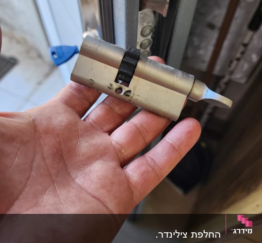 יד מחזיקה צילינדר מנעול ליד דלת פתוחה